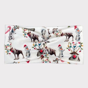 May include: White headband featuring a festive pattern of cartoon reindeer with red noses, snowmen, and colorful Christmas lights. The headband is a twisted style, perfect for holiday wear.