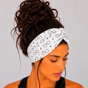 May include: White headband with a black glasses and lightning bolt pattern. The headband is twisted at the top and worn around the forehead. The accessory is made of a soft, stretchy material.