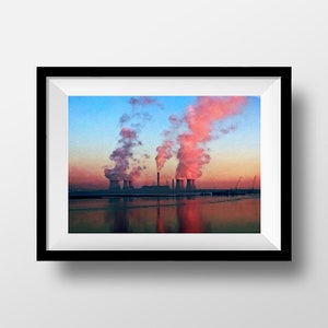 May include: A framed print depicting an industrial landscape at dusk. The artwork shows cooling towers releasing pink smoke against a blue and orange sky. The water below reflects the scene, creating a symmetrical effect.
