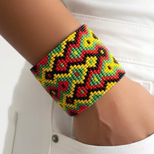 May include: A wide beaded bracelet in a vibrant pattern of red, yellow, green, and black. The cuff bracelet is worn on a wrist, showcasing the intricate beadwork and bold color combination. The bracelet is a statement piece.