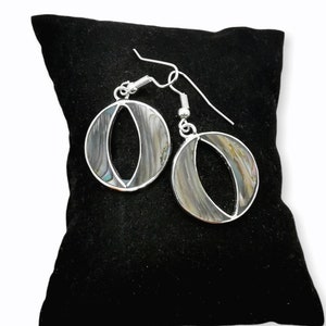 May include: A pair of silver earrings with a circular design featuring a mother-of-pearl inlay. The earrings are displayed on a black velvet cushion.