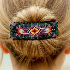 May include: A beaded hair clip in a rectangular shape, featuring a geometric design with pink, orange, white, and green beads. The clip is set against a backdrop of blonde hair styled in a bun.