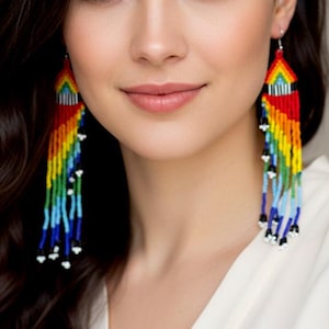 May include: Rainbow beaded earrings with a vibrant array of colors, including red, yellow, green, and blue. The earrings have a geometric design at the top and cascading beaded strands. A colorful and eye-catching accessory.