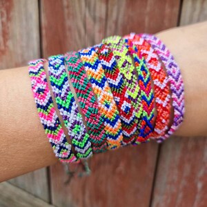 May include: A stack of colorful friendship bracelets with geometric patterns in shades of pink, green, blue, white, and orange.