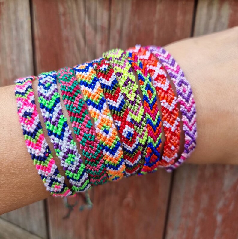 May include: A stack of colorful friendship bracelets with geometric patterns in shades of pink, blue, green, orange, and white.