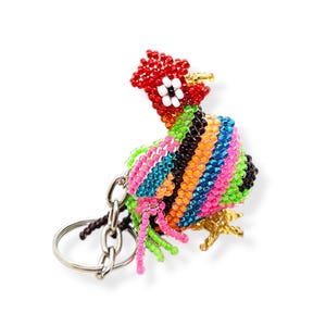 May include: A colorful beaded rooster keychain with a silver key ring. The rooster is made of small, colorful beads in shades of red, orange, yellow, green, blue, and purple. The rooster has a black eye and a gold beak.