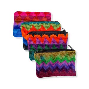 May include: Four crochet zipper pouches in a row. Each pouch features a zig-zag pattern in a different colour scheme, including pink, blue, orange, purple, and green. The pouches have black zippers and are set against a white background.