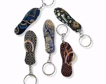 May include: Five colorful flip-flop keychains with silver key rings. The flip-flops are made of fabric with different patterns.
