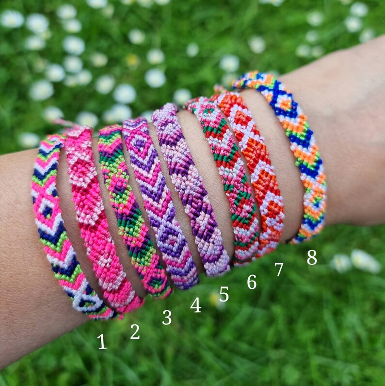May include: Eight colorful friendship bracelets with different patterns, including pink, purple, green, orange, and blue. The bracelets are numbered 1 through 8.