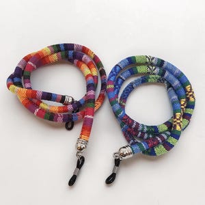 May include: Two eyeglass lanyards. One is a vibrant mix of red, orange, yellow, green, and purple. The other is blue, green, and yellow. Both have silver-toned clasps and black rubber loops for glasses.
