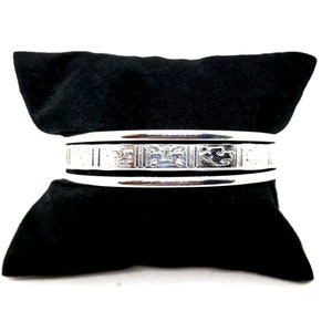 Könnte beinhalten: Silbernes Armreif-Armband mit einem komplizierten gravierten Design. Das Armband liegt auf einem schwarzen Samt-Hintergrund.