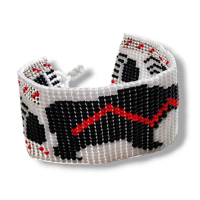 May include: A white beaded bracelet with a black and red design. The design is of a dog, possibly a black lab, with a red collar.
