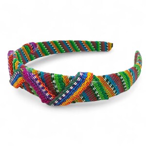 May include: A multi-coloured knotted headband with a striped design. The headband incorporates green, red, blue, orange, and purple shades. The fabric is wrapped around the band, creating a textured and fashionable accessory.