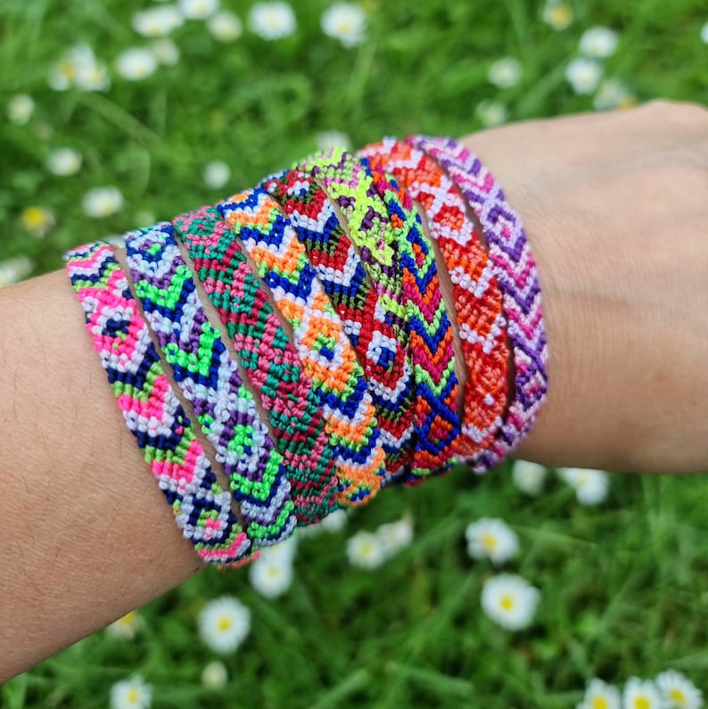 May include: A stack of colorful friendship bracelets with geometric patterns in shades of pink, green, blue, orange, and purple.