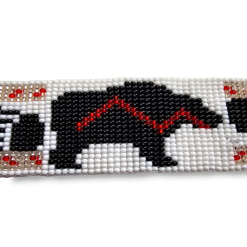 May include: A beaded bracelet with a black and white bear design. The bear is outlined in red beads. The bracelet is made with white, black, and red beads.