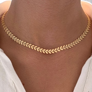 Könnte beinhalten: Eine goldene Kettenkette mit einem blattförmigen Design. Die Kette ist zart und filigran und wäre ein tolles Geschenk für einen Freund oder eine geliebte Person.
