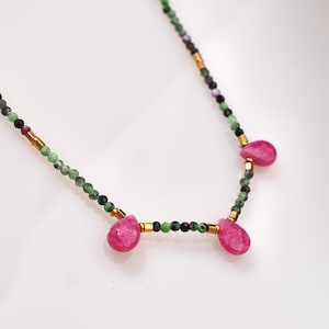 Op de afbeelding: Een delicate ketting met een gouden ketting en groene en zwarte kralen. Drie roze druppelvormige stenen hangen aan de ketting.