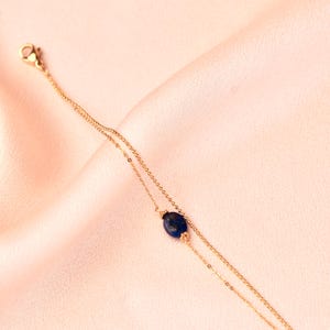 May include: A delicate gold chain bracelet with a single dark blue gemstone pendant.