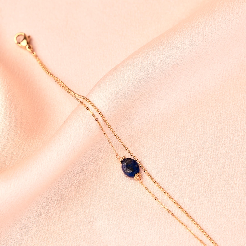 May include: A delicate gold chain bracelet with a single dark blue gemstone pendant.