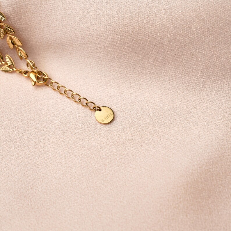 May include: A gold chain necklace with a small leaf design and a tag that reads "S.Steel".