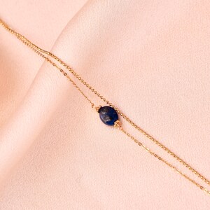 May include: A delicate gold chain necklace with a single, oval-shaped lapis lazuli stone pendant. The necklace is layered with two chains of different thicknesses.