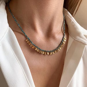 May include: A delicate necklace featuring small turquoise beads and gold-colored, leaf-shaped pendants. The necklace is worn around the neck, showcasing its intricate design and elegant style. The jewelry is a beautiful accessory.