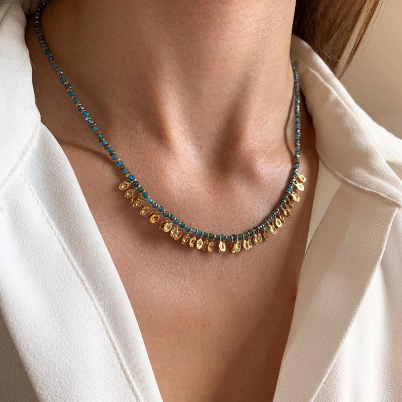 May include: A delicate necklace featuring small turquoise beads and gold-colored, leaf-shaped pendants. The necklace is worn around the neck, showcasing its intricate design and elegant style. The jewelry is a beautiful accessory.
