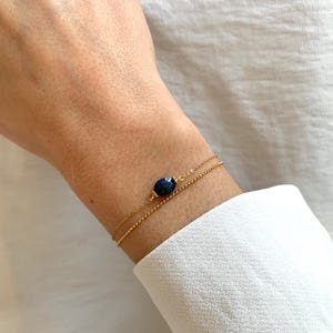 May include: A gold chain bracelet with a dark blue oval gemstone. The bracelet is layered with two chains.