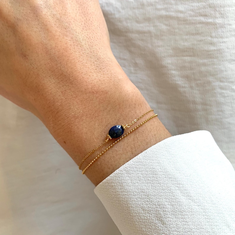 May include: A gold chain bracelet with a dark blue oval gemstone. The bracelet is layered with two chains.