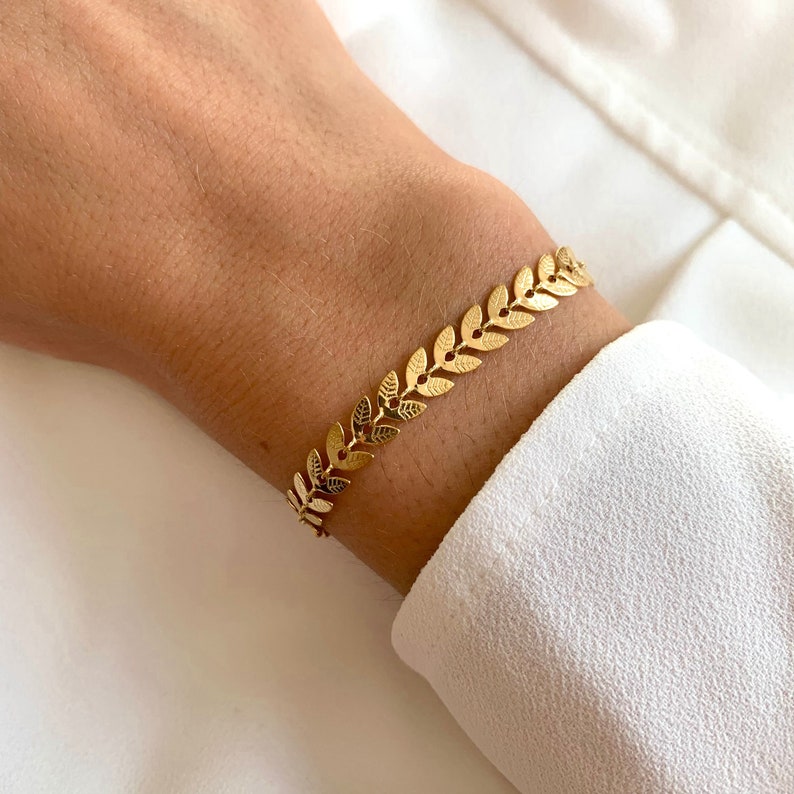 May include: A gold leaf chain bracelet. The bracelet is made of small, interconnected leaf-shaped links.