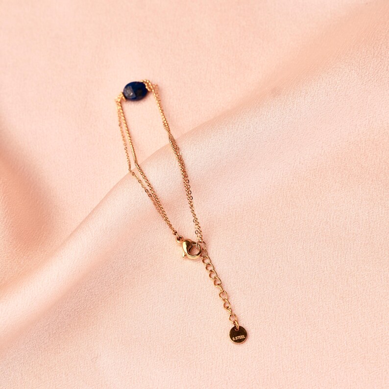 May include: A gold chain bracelet with a dark blue gemstone. The bracelet has a lobster clasp and a small tag that says "S.Steel".