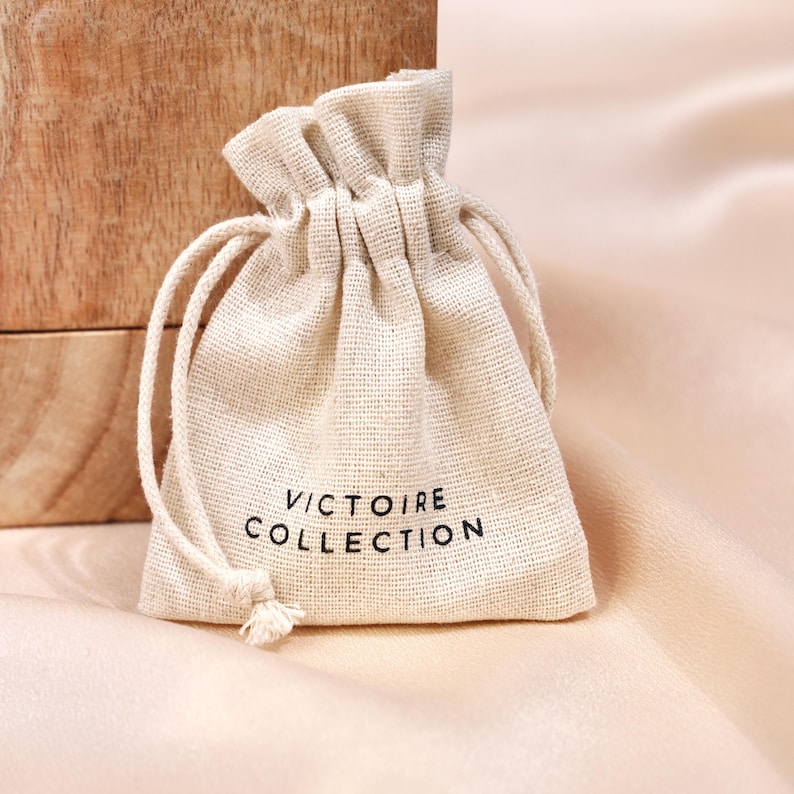 May include: A small, off-white drawstring bag made of natural fabric with the text "Victoire Collection" printed in black.