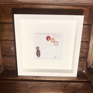 May include: A framed artwork with a white background and a hand-drawn illustration of a person holding balloons. The text "Don't just follow your dreams... Chase them" is written in black ink. The balloons are made of colourful stones.