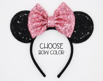 May include: A black headband featuring two round black sequined ears and a large pink sequined bow positioned between them. The text CHOOSE BOW COLOR is printed in black in the centre of the headband, indicating a customisable product option.