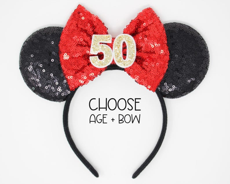 May include: A black headband with two round black sequined ears and a large red sequined bow in the center. The bow features the number 50 in gold glitter. The text CHOOSE AGE + BOW is printed in black on the headband between the ears.