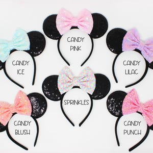 May include: Six black sequin mouse ears headbands with different colored bows. The bows are pink, light blue, peach, lilac, white with rainbow sequins, and pink with white sequins. The headbands are labeled with the names "Candy Pink", "Candy Ice", "Candy Blush", "Candy Lilac", "Sprinkles", and "Candy Punch".