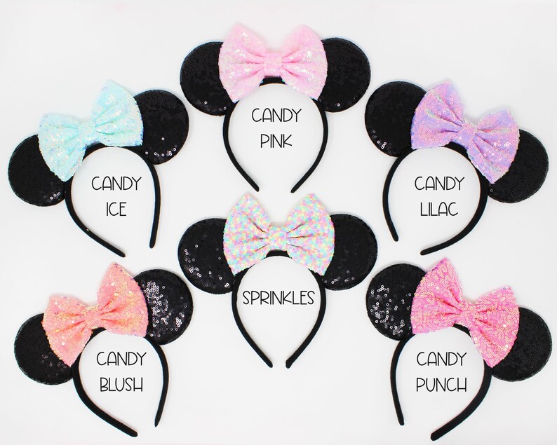 May include: Six black sequin mouse ears headbands with different colored bows. The bows are pink, light blue, peach, lilac, white with rainbow sequins, and pink with white sequins. The headbands are labeled with the names "Candy Pink", "Candy Ice", "Candy Blush", "Candy Lilac", "Sprinkles", and "Candy Punch".