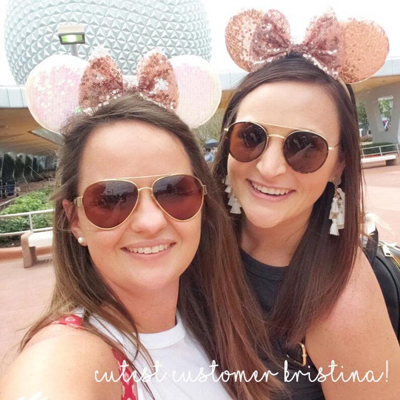 May include: Two friends wearing rose gold Minnie Mouse ears at a theme park. One friend is wearing aviator sunglasses and the other is wearing round sunglasses. The text "cutest customer kristina!" is written on the bottom of the image.