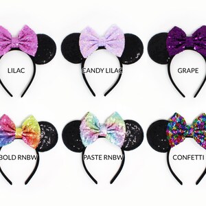 May include: Six headbands with black sequin ears and bows in various colors. The bows are labeled LILAC, CANDY LILAC, GRAPE, BOLD RNBW, PASTE RNBW, and CONFETTI. Each headband features a thin black band and a central sequined bow.
