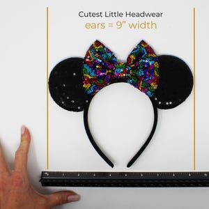 May include: A black headband featuring two round ears covered in black sequins and a central bow decorated with multicolored sequins. Text above the headband reads Cutest Little Headwear ears = 9" width, with a black ruler positioned below.