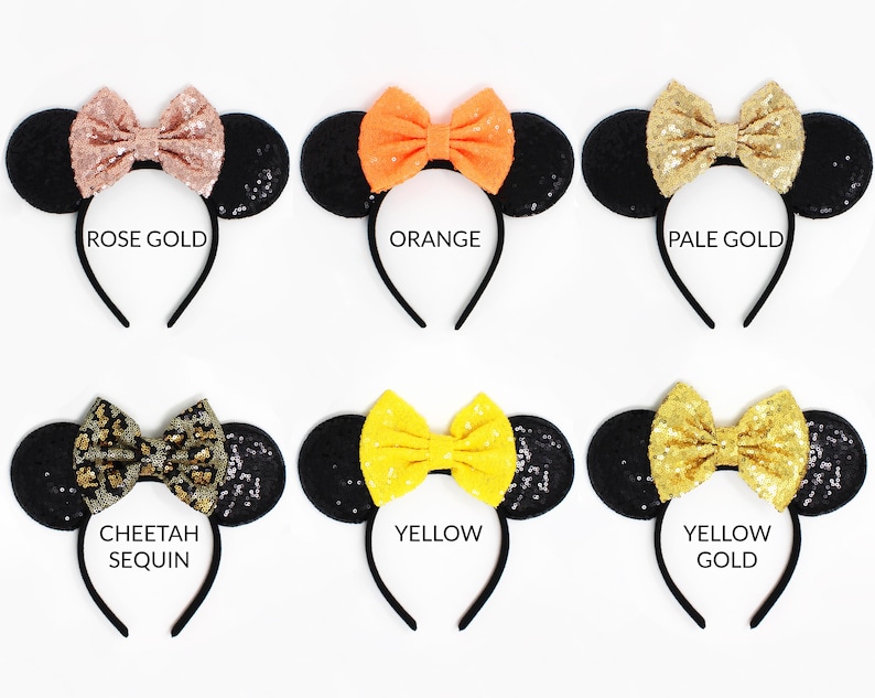 May include: Six headbands with black sequin ears and fabric bows in rose gold, orange, pale gold, cheetah print, yellow, and yellow gold. Each headband features a central bow and round ears, with text labels identifying each color variant below.