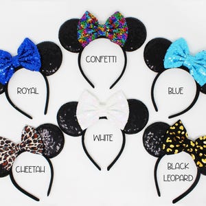 May include: Six pairs of black mouse ears with different colored bows. The bows are confetti, royal blue, blue, white, cheetah print, and black leopard print. The ears are on headbands.