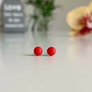 Könnte beinhalten: Ein Paar kleine, runde Ohrstecker in Rot.