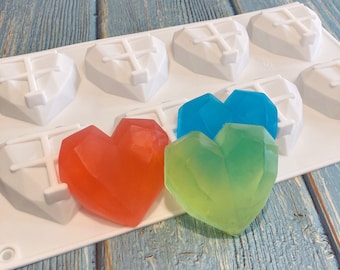May include: A white silicone mold with six heart-shaped cavities, each with a cross design. Three heart-shaped soaps are shown in the mold: one red, one blue, and one green.