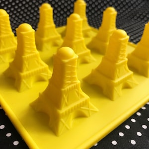 以下が含まれることがあります： 黄色のシリコンモールドで、9つのエッフェル塔の形をした空洞があります。モールドは黒と白のドット柄の表面にあります。