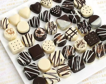 May include: Assortment of chocolate candies in various shapes and sizes, including hearts, squares, circles, and stripes. The chocolates are arranged on a white plate and are a mix of dark and white chocolate.