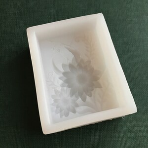 Puede incluir: Molde de silicona blanco con un dise&ntilde;o floral. El molde presenta dos flores grandes con detalles intrincados y peque&ntilde;os acentos florales.