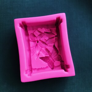 May include: Pink silicone mold with a raised design of a butterfly and flower. The mold is designed for making soap, resin, or other crafts.
