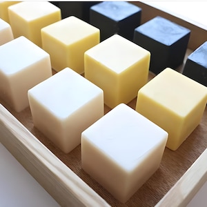 Peut inclure: Un plateau en bois rempli de petits savons carrés de différentes couleurs, dont le blanc, le jaune et le noir.