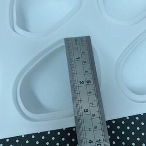 Puede incluir: Primer plano de un molde de silicona blanco con m&uacute;ltiples cavidades ovaladas. Una regla se coloca al lado del molde, mostrando que el tama&ntilde;o de las cavidades es de aproximadamente 5 cm de largo.